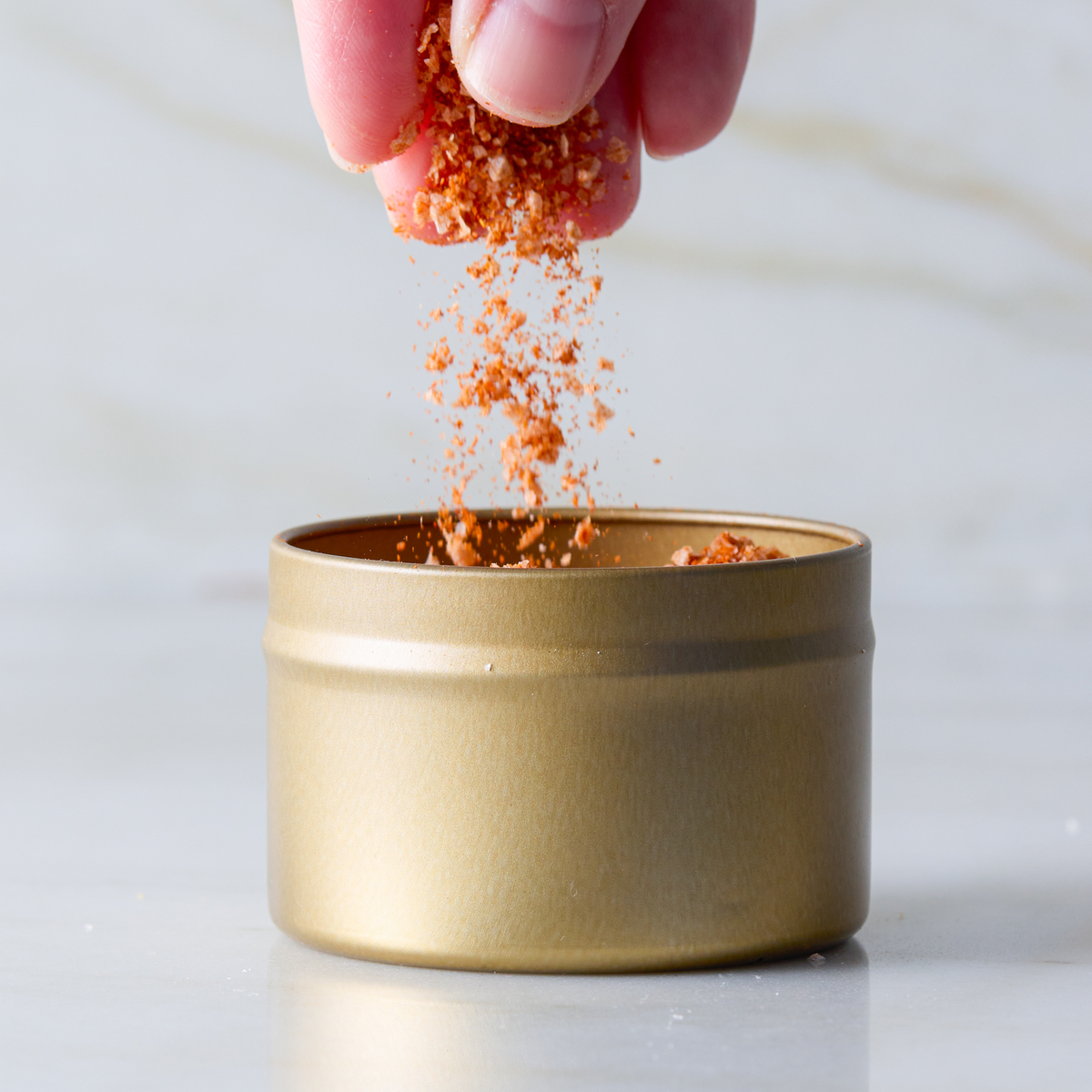 a hand pouring red spice from a small container